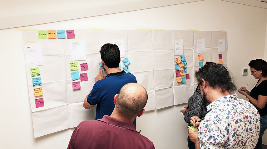 Gruppo di persone davanti a un cartellone mentre scrivono e attaccano post-it